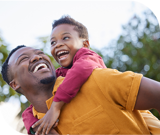 Man with a large smile holds his son on his back, who is also smiling.